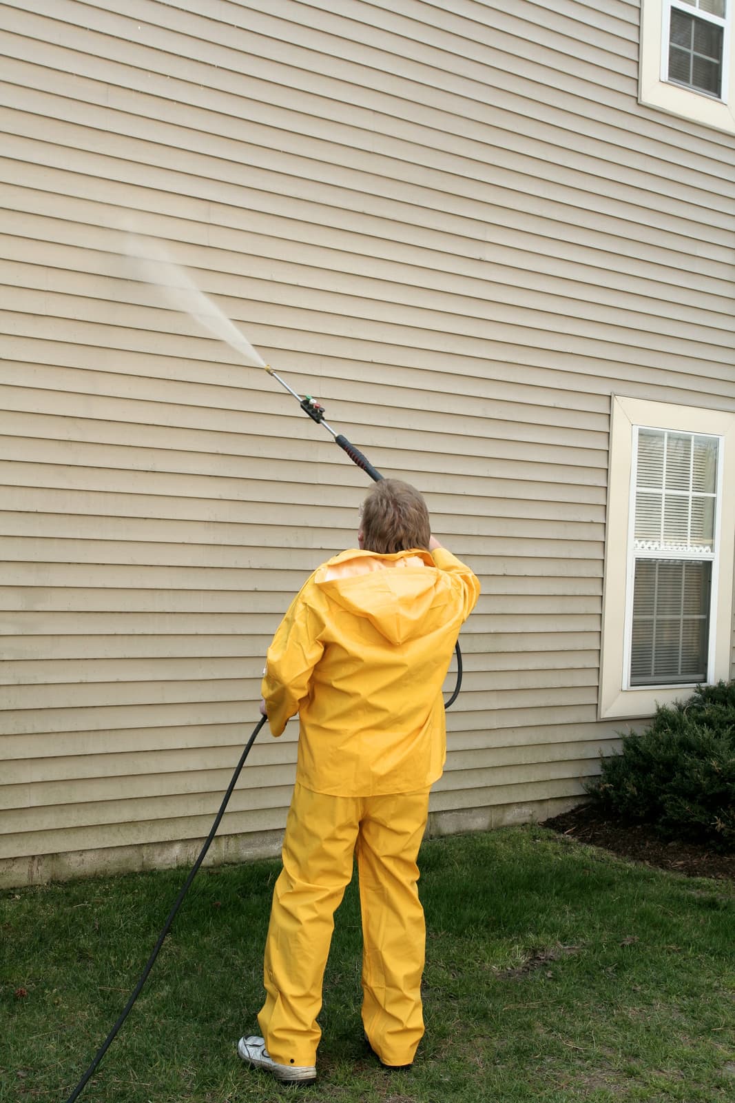 Worker pressure washing tan house siding